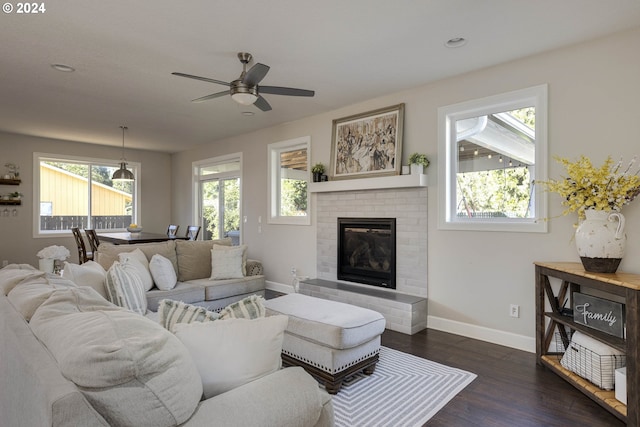 living room with dark wood-type flooring, a brick fireplace, and ceiling fan