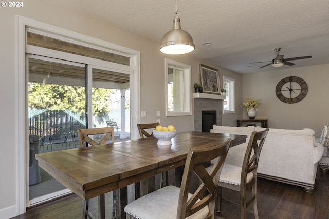 dining space featuring dark wood-type flooring, a fireplace, a textured ceiling, and ceiling fan