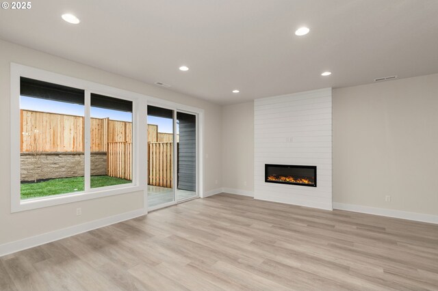 unfurnished living room featuring recessed lighting, a large fireplace, light wood finished floors, baseboards, and visible vents