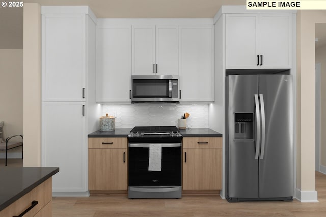 kitchen with dark countertops, decorative backsplash, light wood-style flooring, and appliances with stainless steel finishes