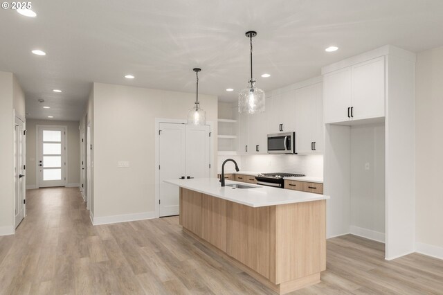 kitchen featuring recessed lighting, stainless steel appliances, a sink, baseboards, and a center island with sink