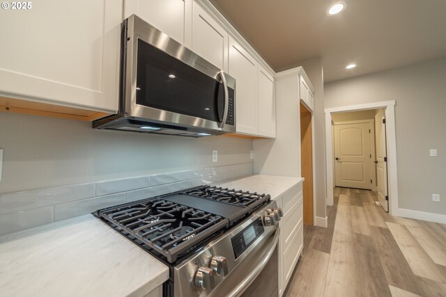 kitchen with white cabinets, light wood-type flooring, and appliances with stainless steel finishes