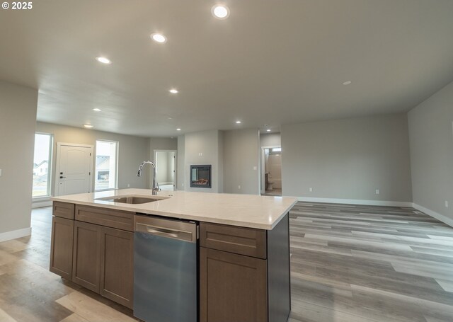 kitchen featuring an island with sink, stainless steel dishwasher, light hardwood / wood-style floors, and sink