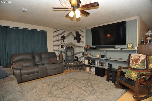 living room featuring ceiling fan, a wood stove, a textured ceiling, and light hardwood / wood-style flooring