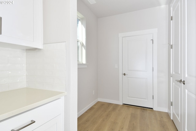 interior space with baseboards, light wood finished floors, decorative backsplash, light countertops, and white cabinetry