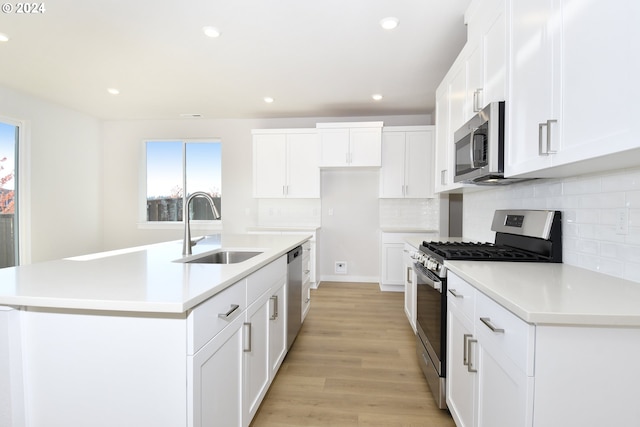 kitchen with stainless steel appliances, a kitchen island with sink, sink, light hardwood / wood-style flooring, and white cabinetry