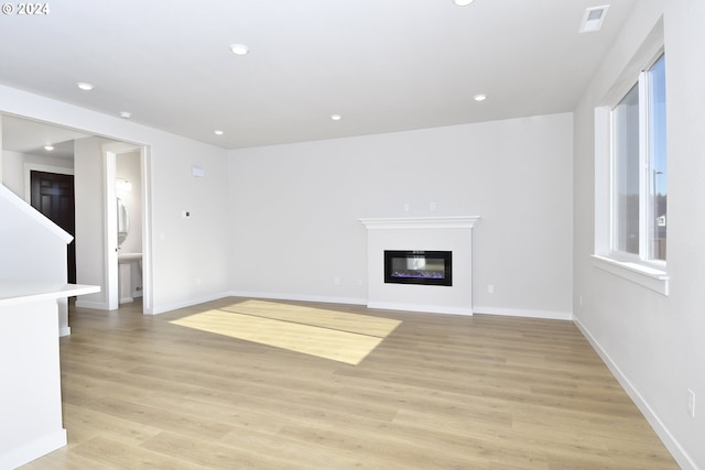 unfurnished living room with recessed lighting, light wood-style flooring, and a glass covered fireplace