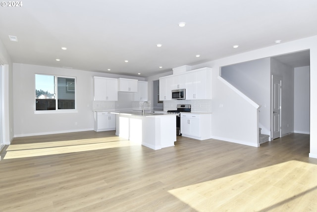 kitchen featuring a center island with sink, stainless steel appliances, open floor plan, and light wood-style flooring