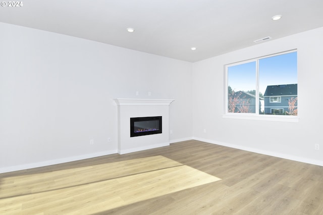 unfurnished living room with recessed lighting, baseboards, light wood-style floors, and a glass covered fireplace