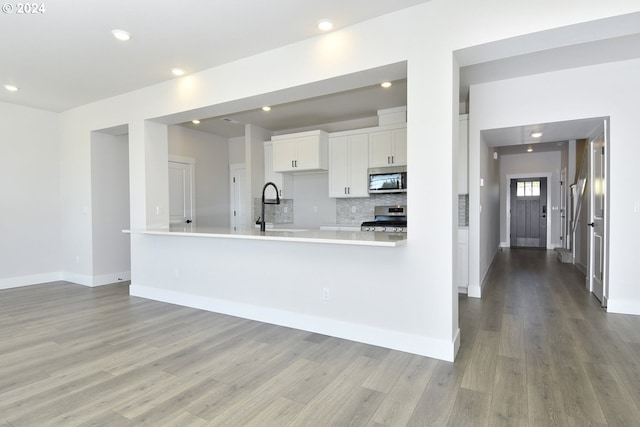 kitchen with sink, light hardwood / wood-style flooring, white cabinetry, kitchen peninsula, and stainless steel appliances