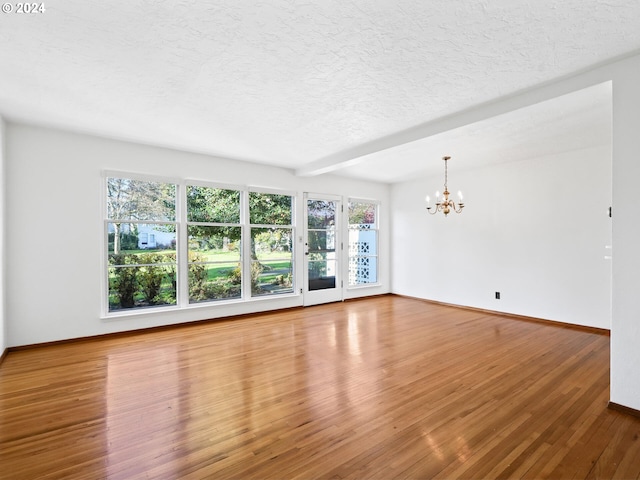 empty room with beam ceiling, wood-type flooring, a textured ceiling, and an inviting chandelier