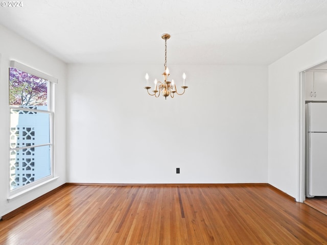 unfurnished room with hardwood / wood-style floors, a textured ceiling, and a notable chandelier