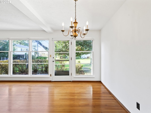 unfurnished dining area featuring hardwood / wood-style flooring, a textured ceiling, beamed ceiling, and an inviting chandelier