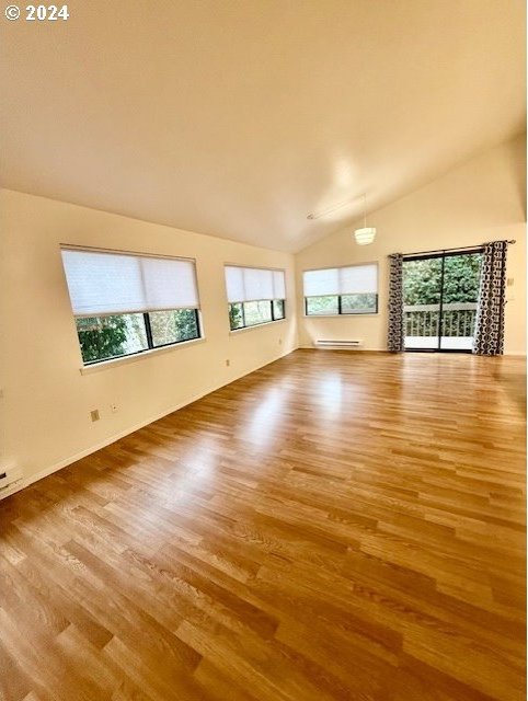 unfurnished living room with hardwood / wood-style flooring, high vaulted ceiling, a baseboard radiator, and a healthy amount of sunlight