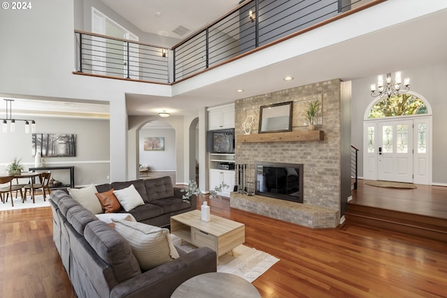 living room with hardwood / wood-style flooring, a chandelier, a high ceiling, and a brick fireplace