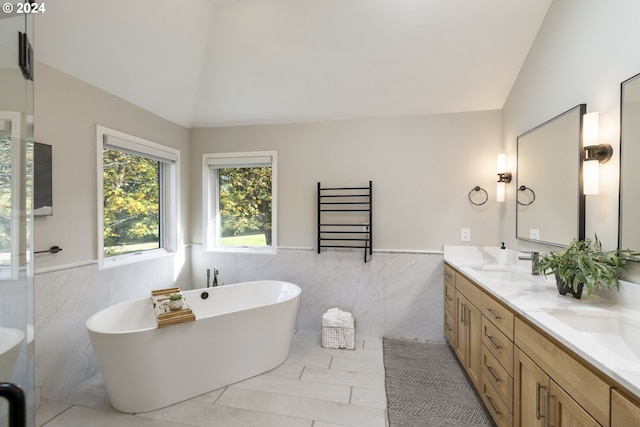 bathroom with tile walls, vaulted ceiling, a bath, vanity, and tile patterned flooring