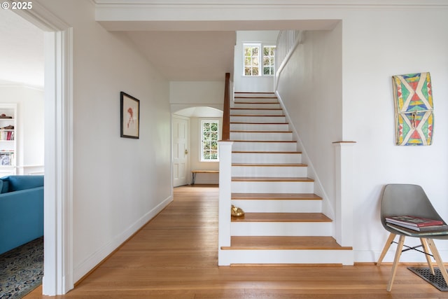 stairs with baseboards, plenty of natural light, arched walkways, and wood finished floors