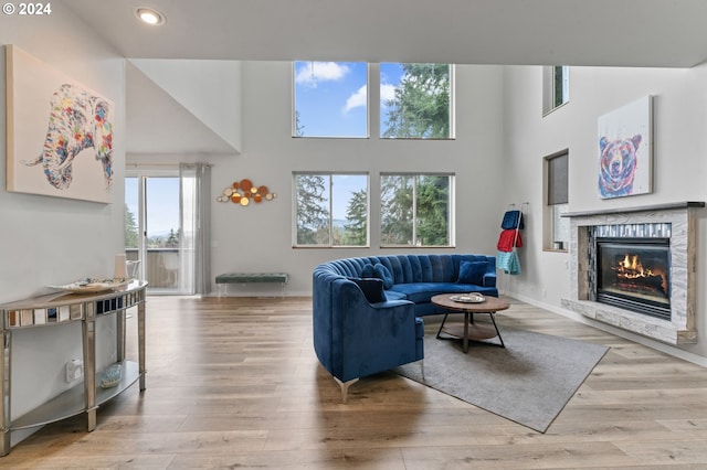 living room with a towering ceiling, a stone fireplace, and light hardwood / wood-style flooring