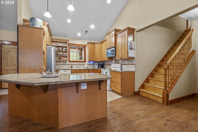 kitchen with vaulted ceiling, sink, light stone counters, decorative backsplash, and appliances with stainless steel finishes