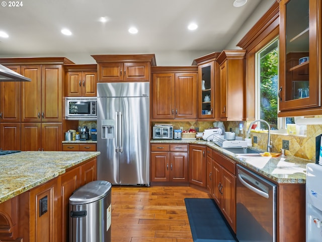 kitchen featuring light hardwood / wood-style floors, tasteful backsplash, sink, light stone countertops, and built in appliances