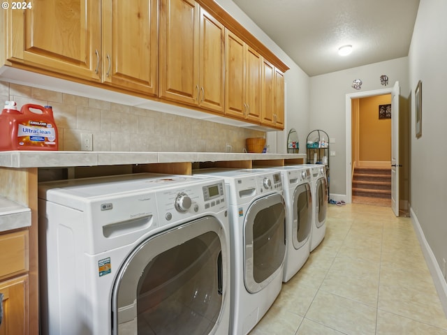 washroom featuring washing machine and dryer, cabinets, light tile patterned flooring, and a textured ceiling