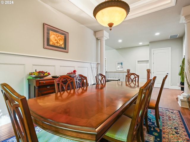 dining room with hardwood / wood-style floors, ornate columns, and crown molding