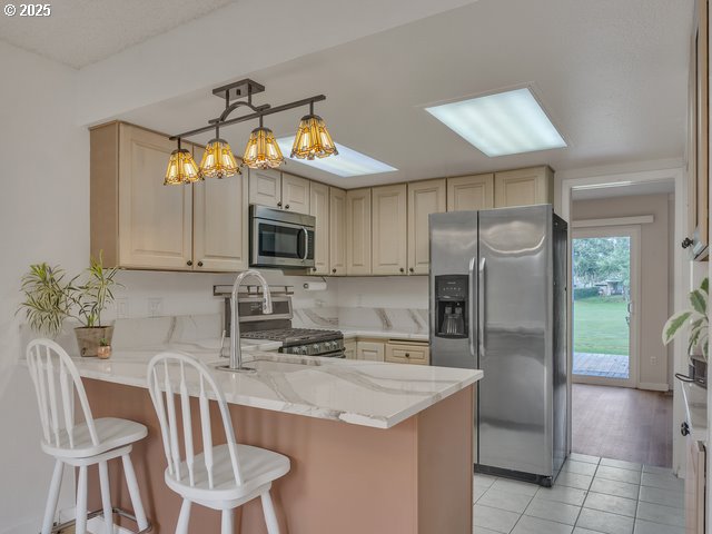 kitchen with light tile patterned flooring, a breakfast bar area, light stone counters, kitchen peninsula, and stainless steel appliances