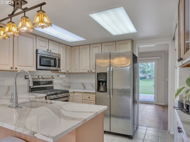 kitchen with pendant lighting, light stone countertops, kitchen peninsula, and appliances with stainless steel finishes