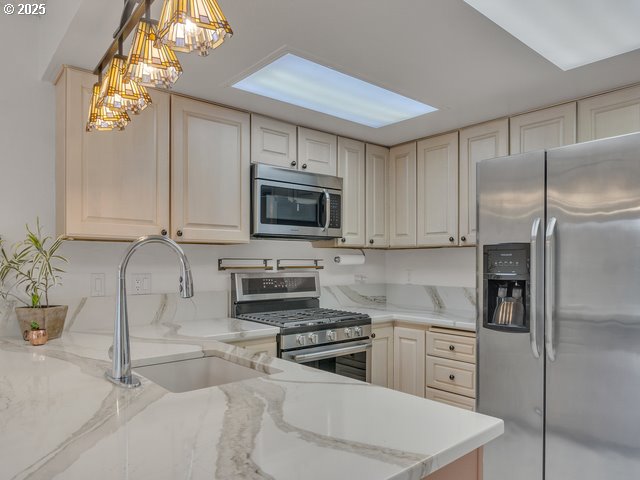 kitchen with hanging light fixtures, light stone countertops, appliances with stainless steel finishes, and sink