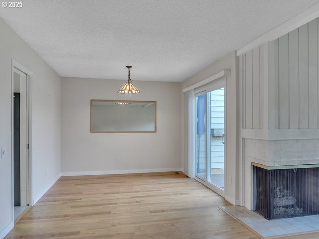 unfurnished dining area featuring a brick fireplace, light hardwood / wood-style flooring, and a textured ceiling