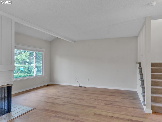 unfurnished living room with a multi sided fireplace, lofted ceiling with beams, a textured ceiling, and light wood-type flooring