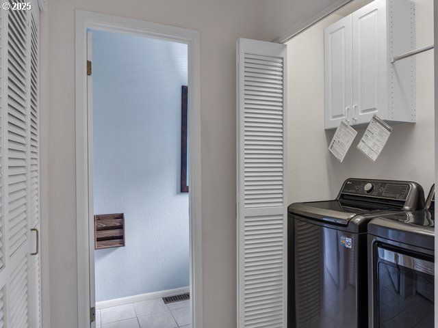 laundry area featuring independent washer and dryer, light tile patterned floors, and cabinets