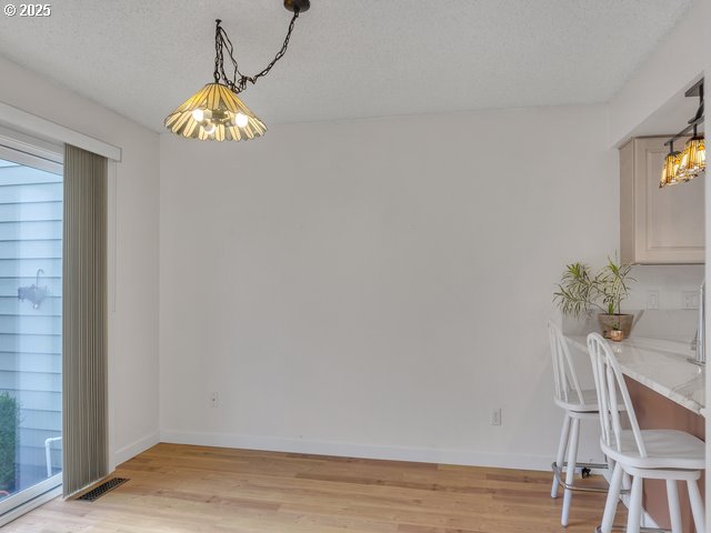 unfurnished dining area featuring an inviting chandelier, a textured ceiling, and light wood-type flooring