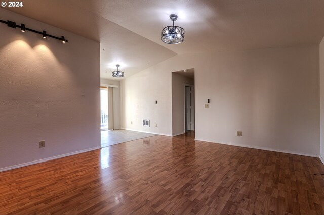 empty room featuring lofted ceiling, dark wood-type flooring, and an inviting chandelier