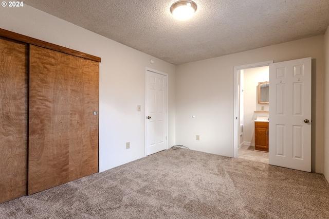 unfurnished bedroom featuring connected bathroom, light carpet, a closet, and a textured ceiling