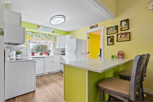 kitchen featuring tasteful backsplash, kitchen peninsula, white appliances, a breakfast bar, and white cabinets