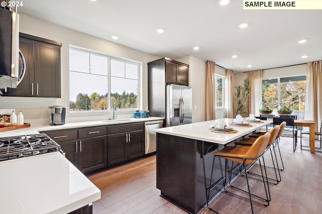 kitchen with sink, a center island, stainless steel appliances, a kitchen bar, and light wood-type flooring