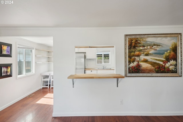 kitchen with white cabinets, kitchen peninsula, stainless steel refrigerator, hardwood / wood-style flooring, and a breakfast bar area