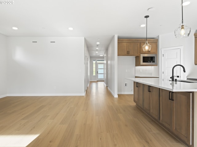 kitchen featuring decorative light fixtures, a center island with sink, light hardwood / wood-style floors, sink, and black microwave