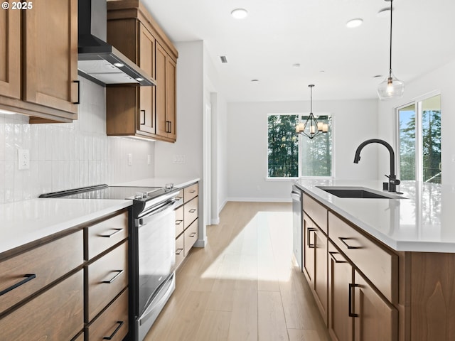 kitchen with pendant lighting, appliances with stainless steel finishes, wall chimney exhaust hood, sink, and light hardwood / wood-style flooring