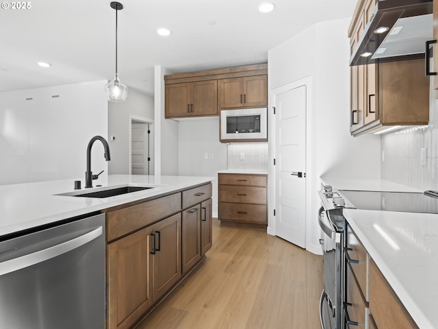 kitchen with range hood, pendant lighting, sink, light hardwood / wood-style flooring, and appliances with stainless steel finishes