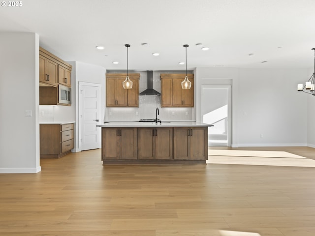 kitchen featuring hanging light fixtures, wall chimney exhaust hood, stainless steel microwave, and light hardwood / wood-style floors