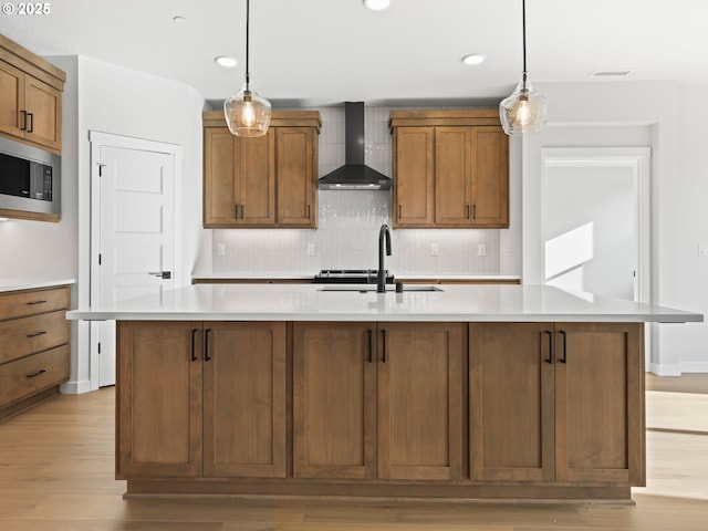 kitchen with sink, wall chimney exhaust hood, hanging light fixtures, and a kitchen island with sink