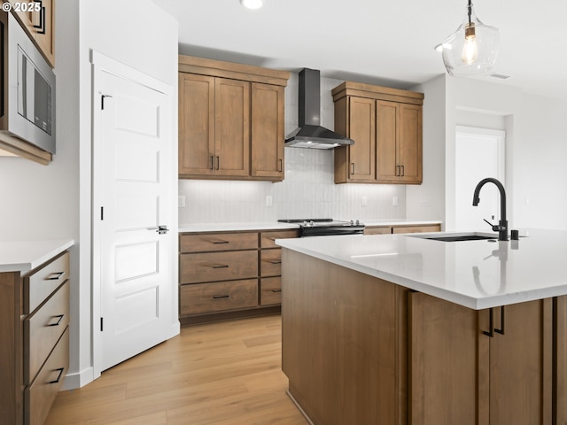 kitchen featuring light hardwood / wood-style floors, stainless steel microwave, decorative light fixtures, wall chimney exhaust hood, and sink