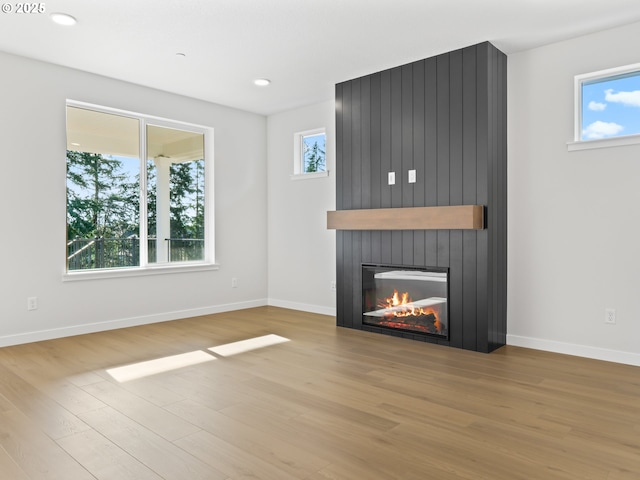 unfurnished living room featuring light hardwood / wood-style floors, a large fireplace, and a healthy amount of sunlight