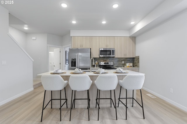 kitchen featuring appliances with stainless steel finishes, tasteful backsplash, a kitchen island with sink, a breakfast bar, and light hardwood / wood-style floors