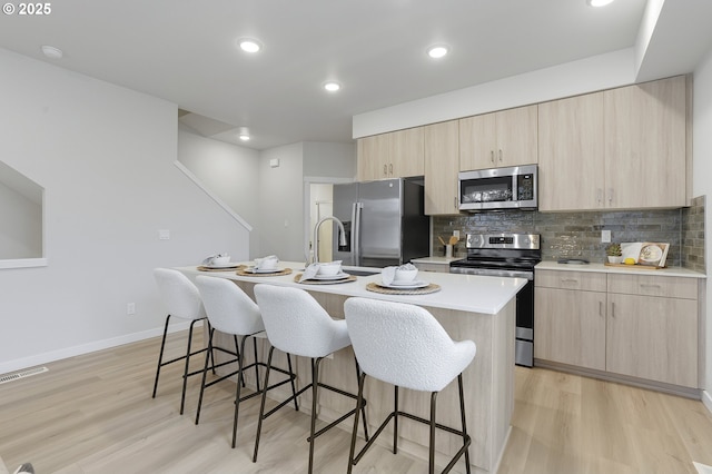 kitchen with light wood-type flooring, a center island with sink, tasteful backsplash, and appliances with stainless steel finishes