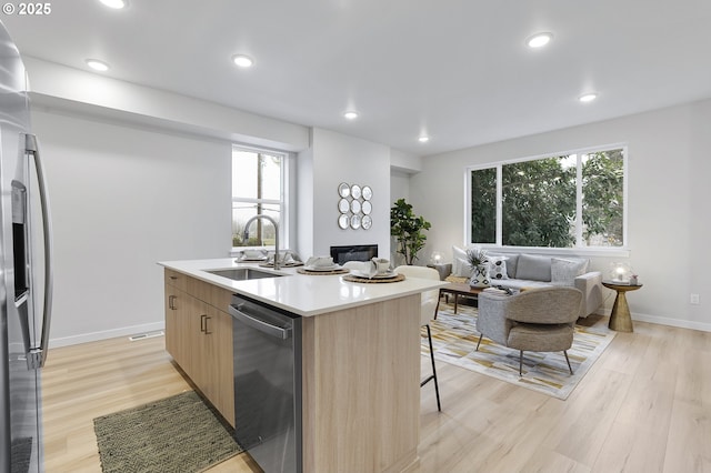 kitchen with appliances with stainless steel finishes, a breakfast bar, sink, a kitchen island with sink, and light hardwood / wood-style floors