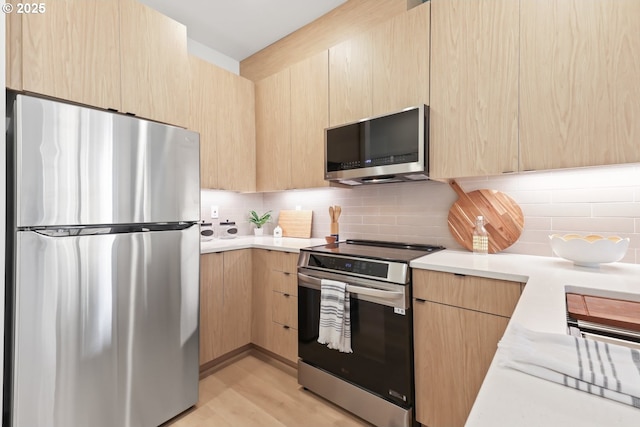 kitchen featuring appliances with stainless steel finishes, light wood-type flooring, backsplash, and light brown cabinetry