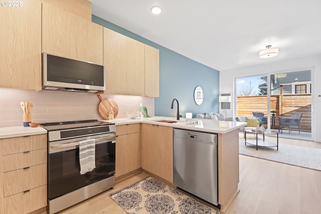 kitchen with sink, appliances with stainless steel finishes, light hardwood / wood-style floors, light brown cabinetry, and kitchen peninsula